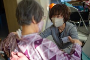 マスク姿の西山智香先生が、車いすに座る方に着付けの指導をしている様子